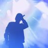 Young rap singer with mic in hand singing popular song in stage in bright blue lights.Hip hop artist performing live on scene in music hall.Youth entertainment event in nightclub.Professional vocalist